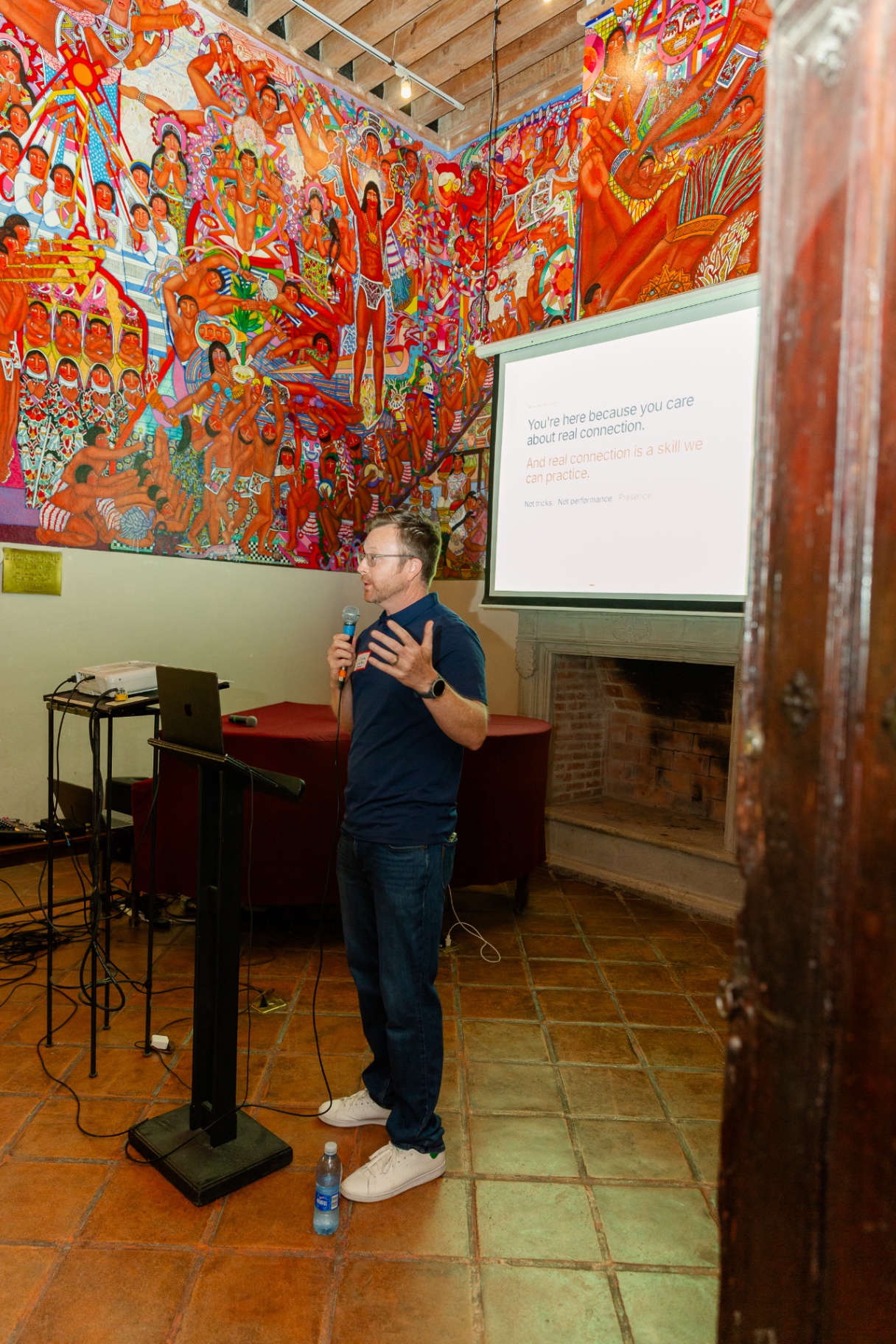 Elisha Goldstein speaking at a live event in a room with a painted mural